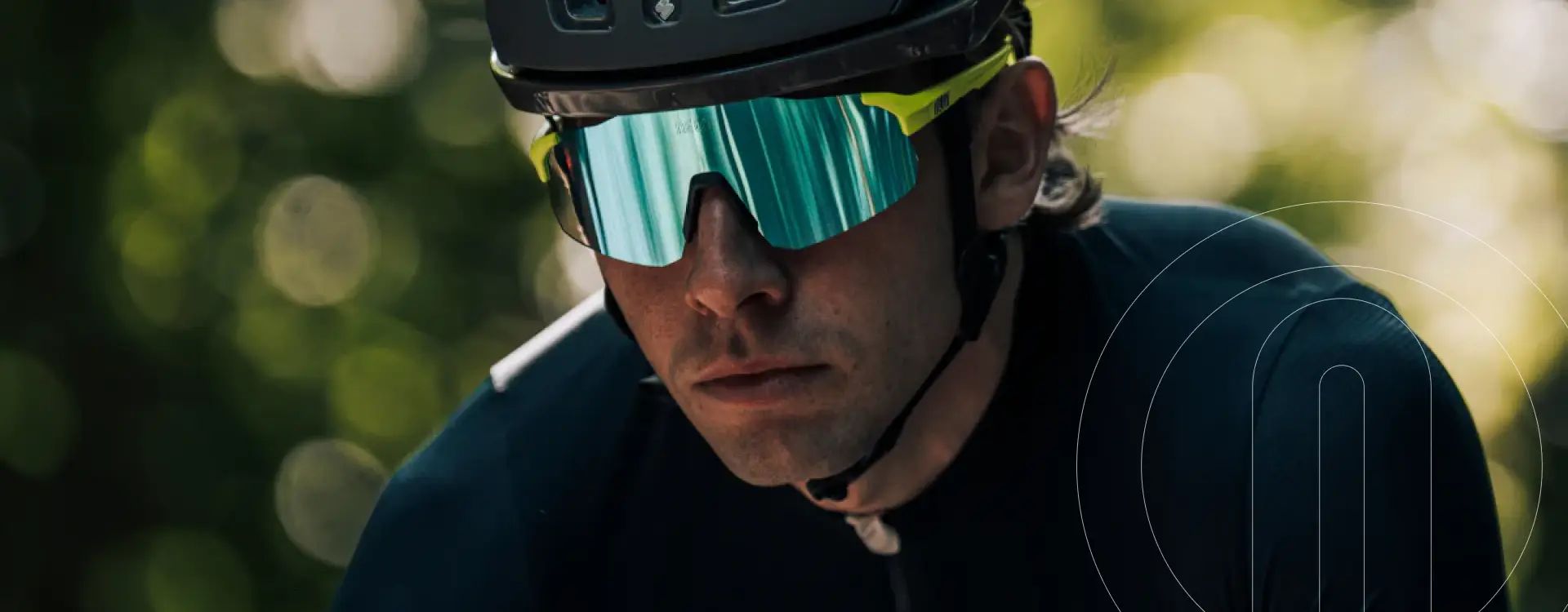 Man in a black cycling helmet and blue-green mirrored NEON sport glasses, wearing a black cycling jersey