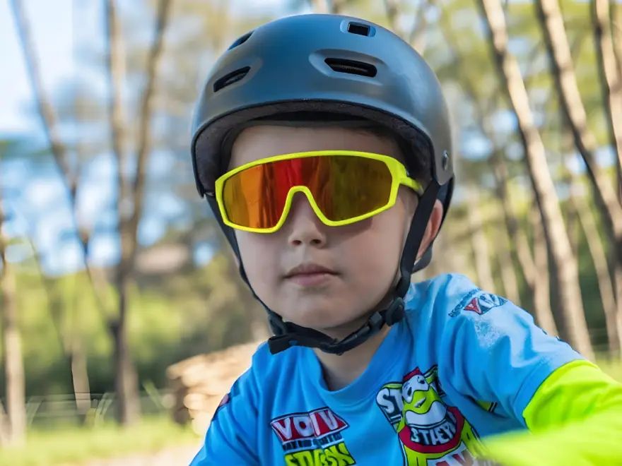 Child in a blue cycling helmet and yellow-orange NEON OPTIC kids' glasses, wearing a blue jersey